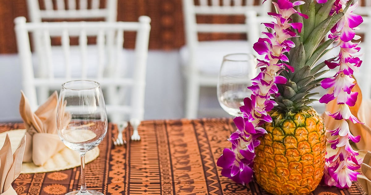 A pineapple dressed with purple orchid lei on a set Maui dining table