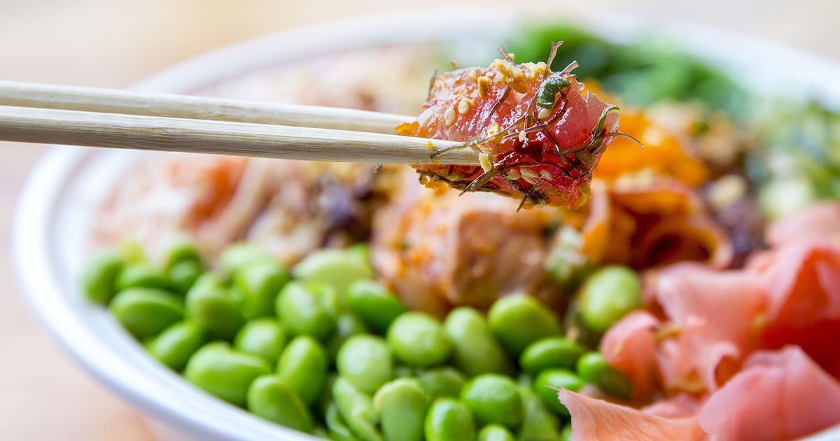 Chopsticks lifting seasoned ahi poke from a colorful bowl