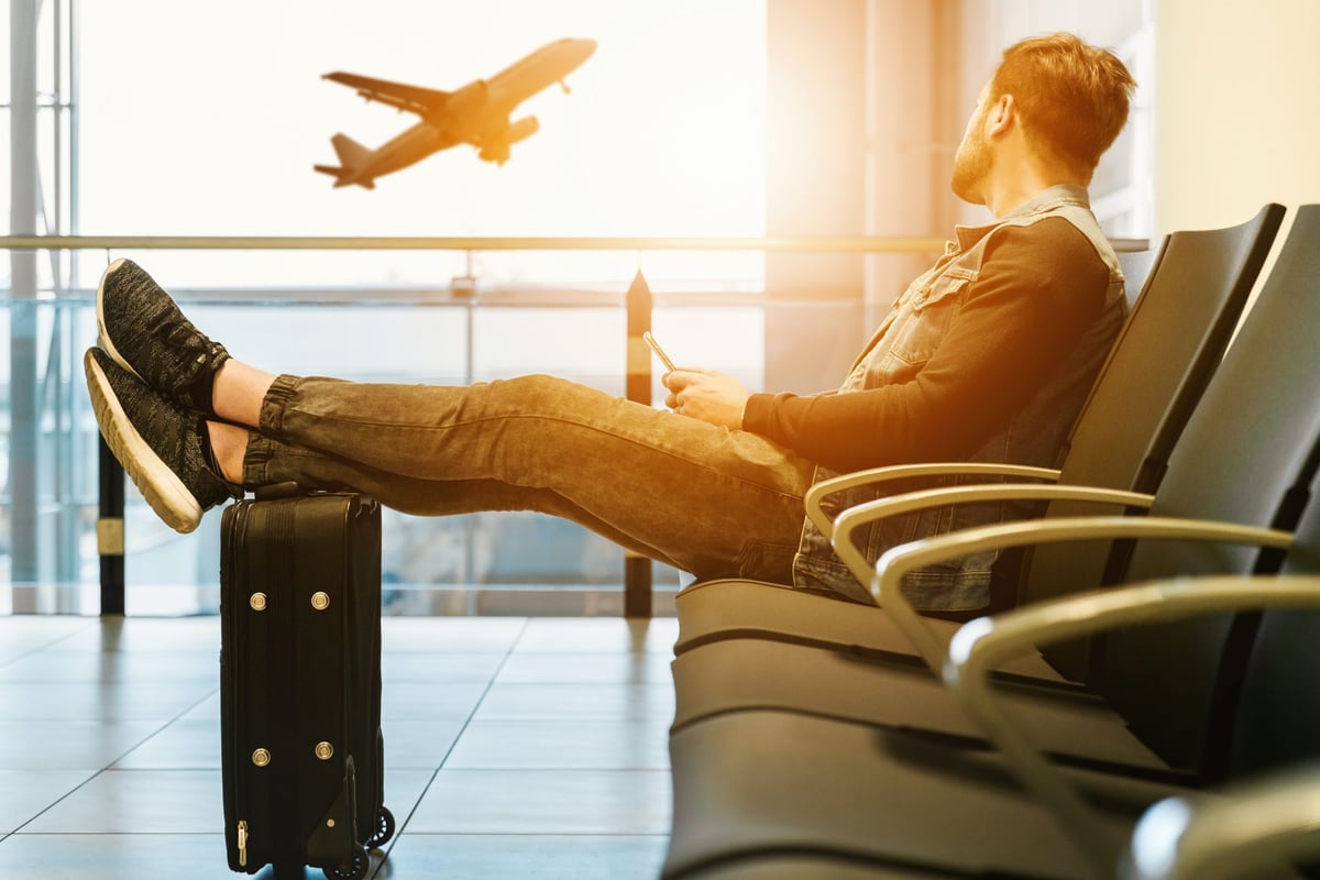 A traveler seated beside a suitcase while an airplane takes off outside the terminal