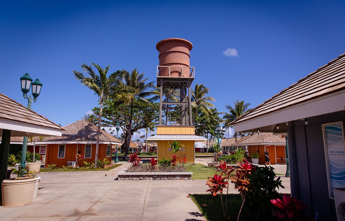 The open-air courtyard at Coconut Marketplace on Kauai, with plantation-style shop buildings, palm trees, and a replica water tower