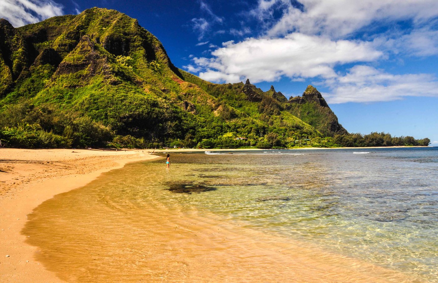 A woman wading into the water near Makua and Tunnels with the North Shore Kauai ridgeline behind her