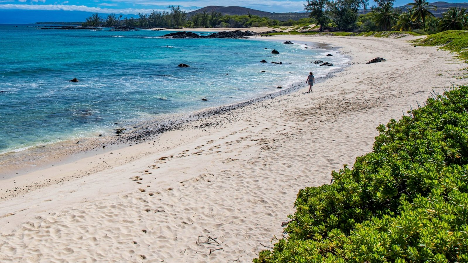Tori walking alone across the white sand at Makalawena Beach on the Big Island