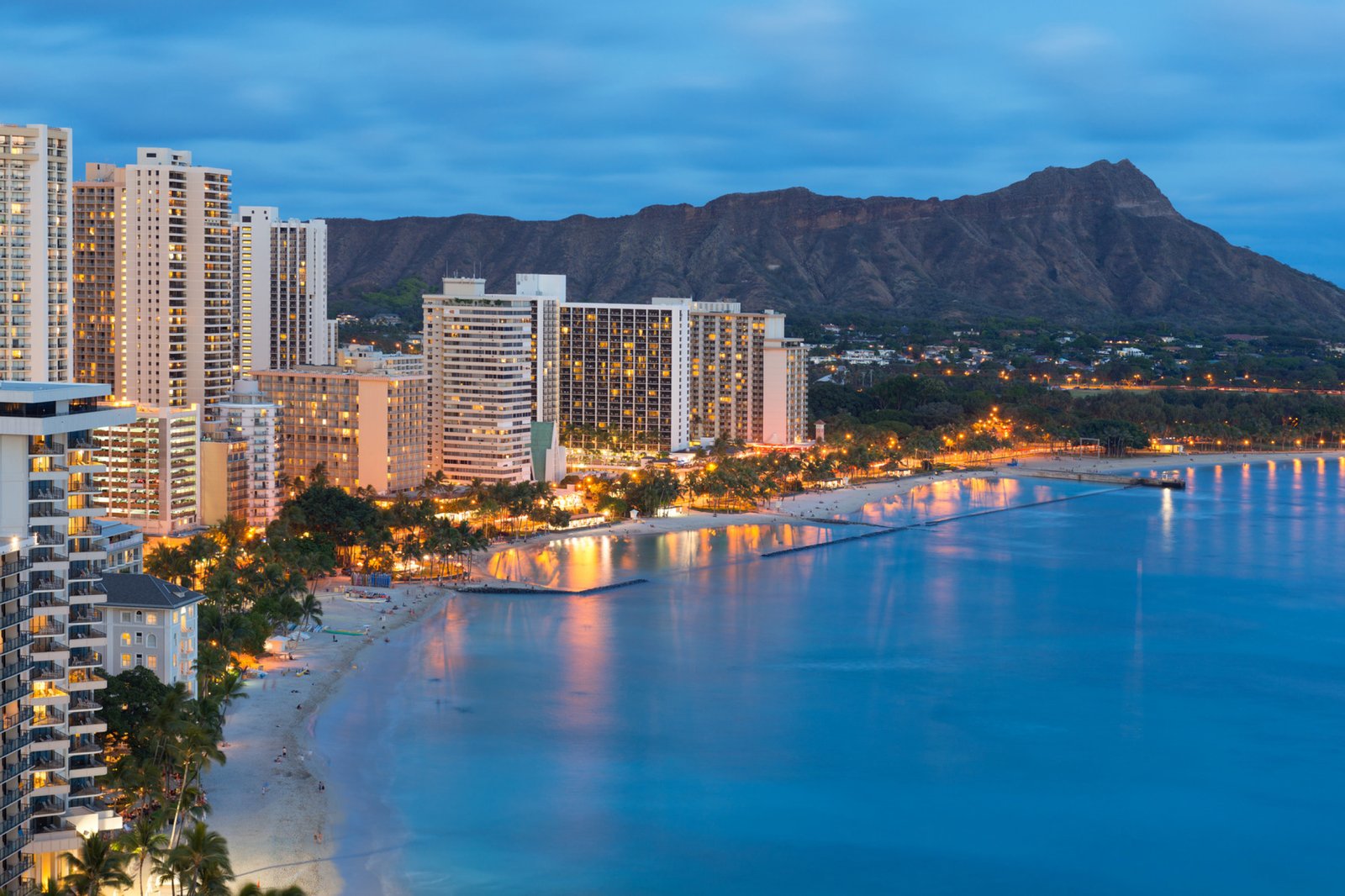 Waikīkī beach and the Honolulu hotel strip on a bright afternoon — most mainland flights land hours before check-in opens.