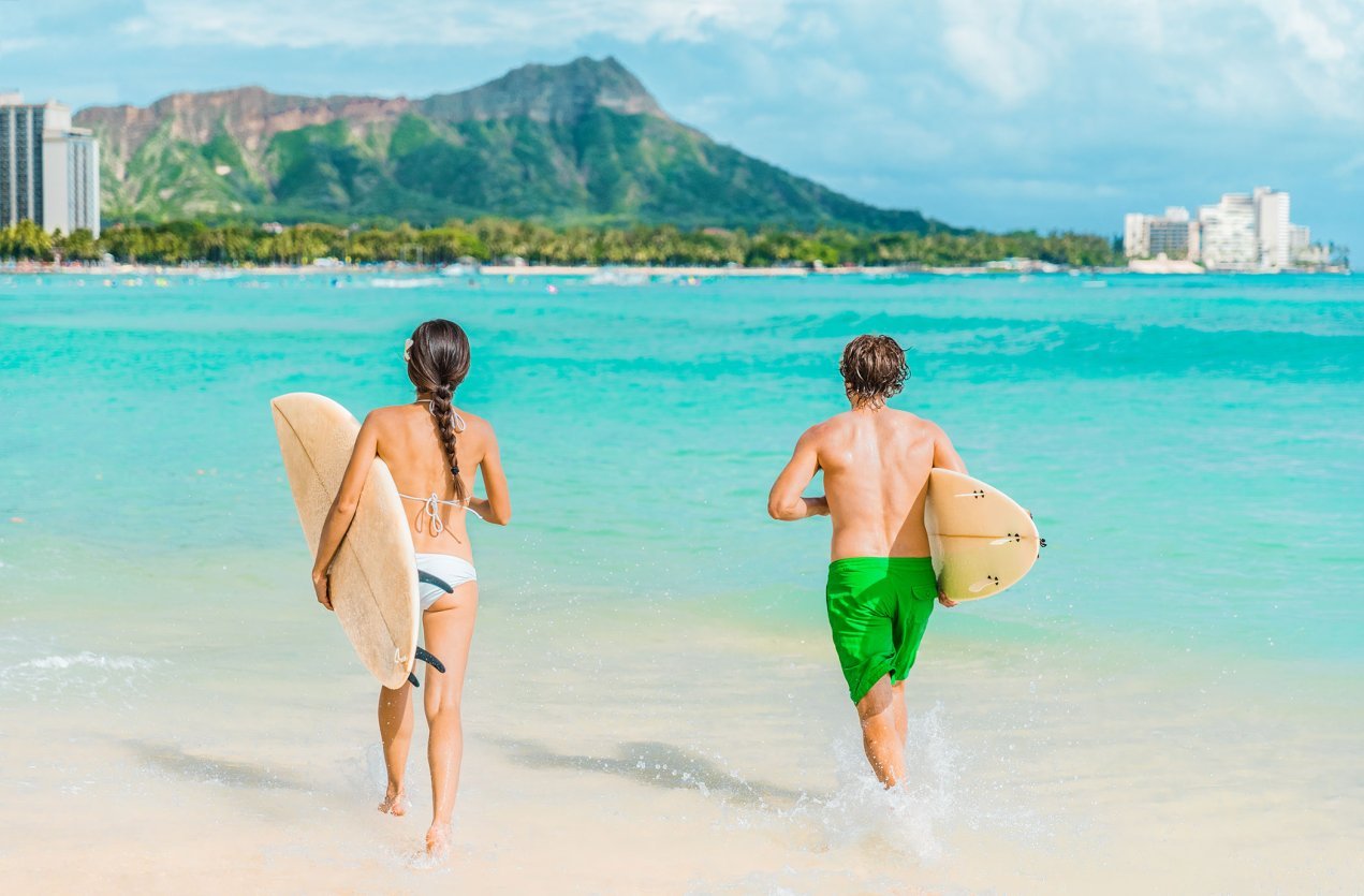 Family with longboards on Waikiki Beach on Oʻahu, Diamond Head rising in the distance.