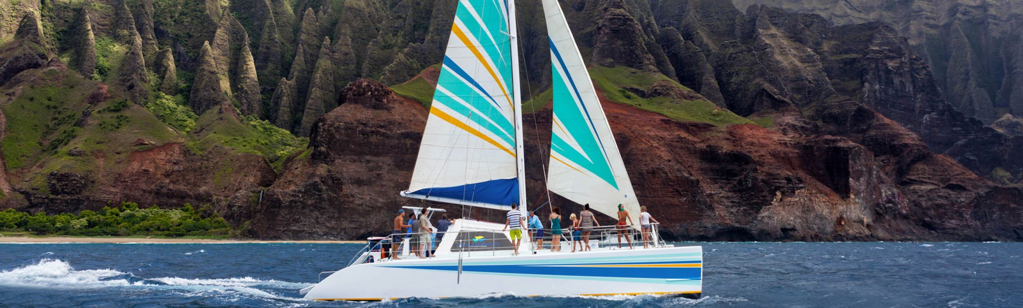 A sailboat with full sails along the Hawaiian coastline.