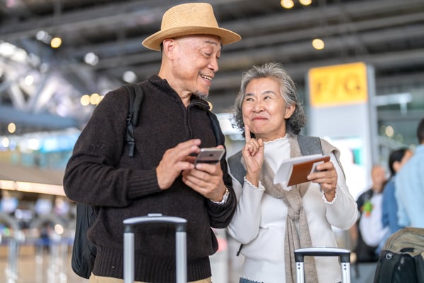 An older couple at an airport checking travel plans on a phone with passports in hand