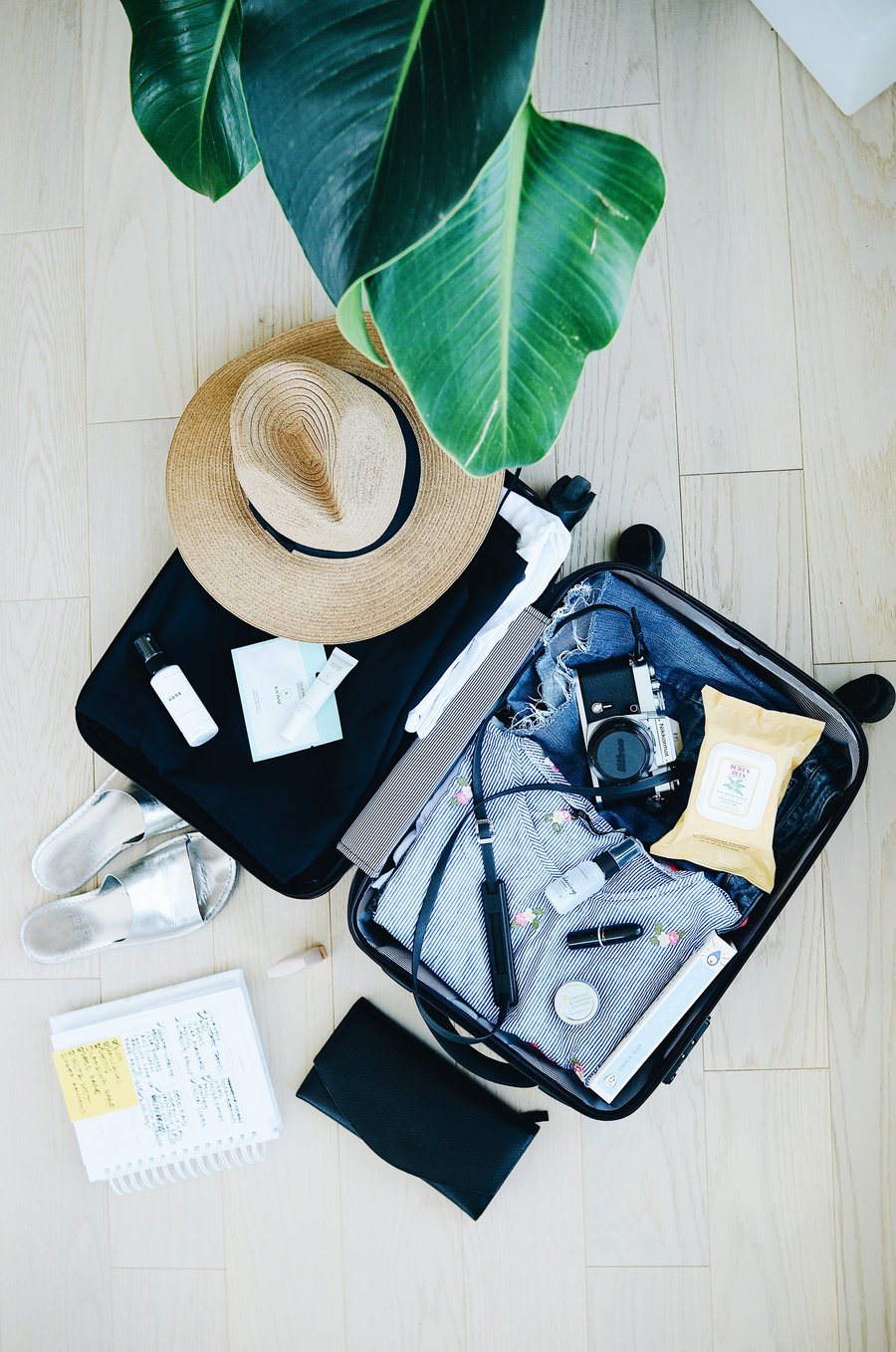 Open suitcase packed with clothing, a sun hat, camera, notebook, and travel essentials