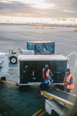Two people working with bags at the airport loading bags onto the plane.