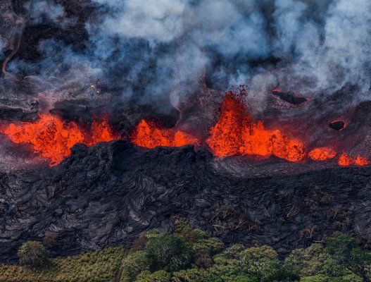 Aerial shot of the Kilauea East Rift Zone Eruption in 2018 with cooled lava meeting the trees, hot lava at the top and smoke billowing.