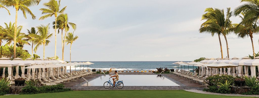 Person riding a bike near the swimming pool and cabanas at the the Four Seasons Resort Hualalai on Big Island.