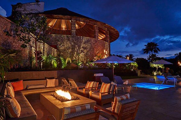 Night time relaxing area with luxury chairs, fireplace, pool and lighted cabana at Hotel Wailea in Maui.