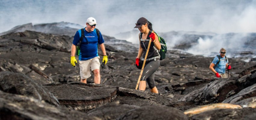 Three people exploring the fresh igneous rock formed from a recent volcano eruption in the National Park.