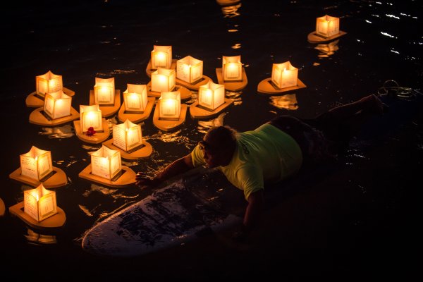 A man floating on a surfboard with lanterns in the water to represent the Lantern Floating Festival a Hawaiian celebration to attend