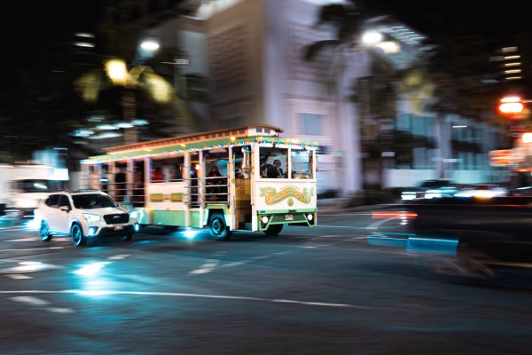 Multiple cars and a trolley going through the streets of Waikiki Hawaii at night.