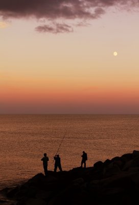 Three people fishing on the rocks at Black Rock Pu’u Keka’a with the sunset in the background