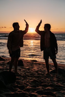 Two people high-fiving on a Hawaiian beach with the sunset and water in the background.