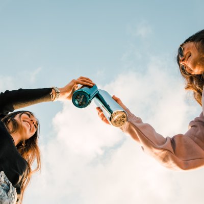 Two women with drinks in water bottles to represent some of the little things that you should bring when packing for Hawaii