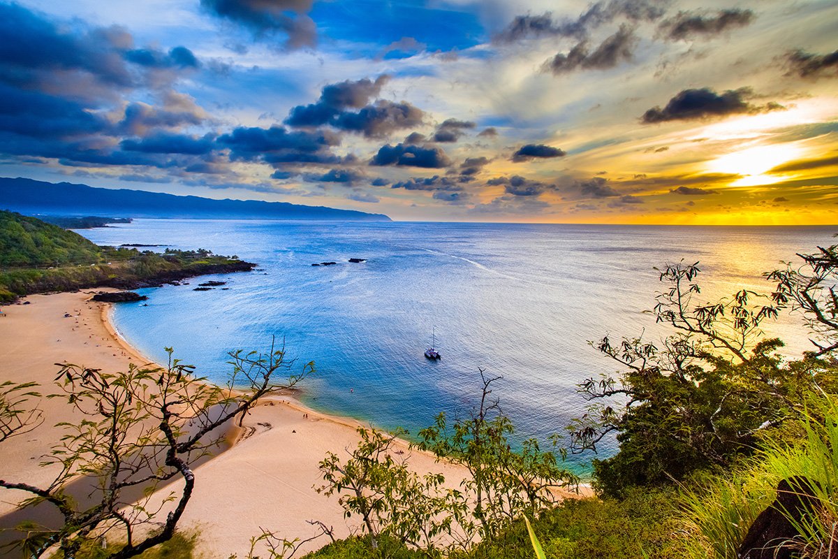Waimea Bay on Oʻahu's North Shore, turquoise water and a curve of sand framed by green hills — the summer face of a coast better known for winter surf.
