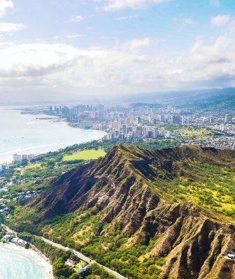 Aerial shot of mountains on the coast with Honolulu in the background.